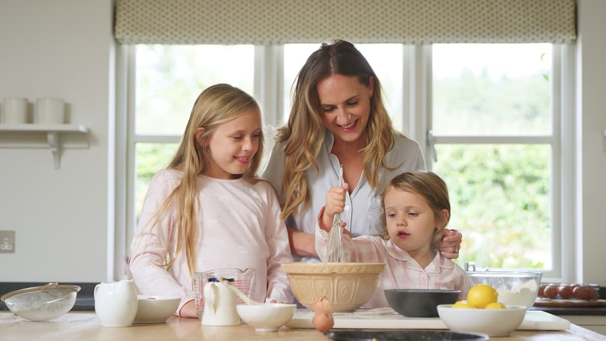 A mom and two kids whisking batter together in a bright kitchen